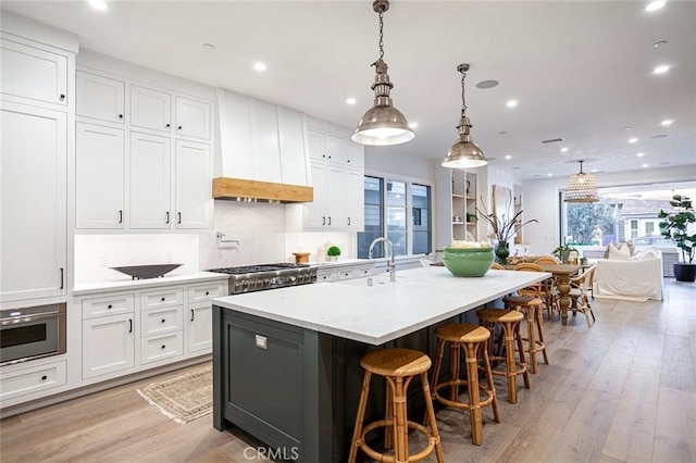 kitchen with premium range hood, decorative light fixtures, white cabinetry, a large island with sink, and stove