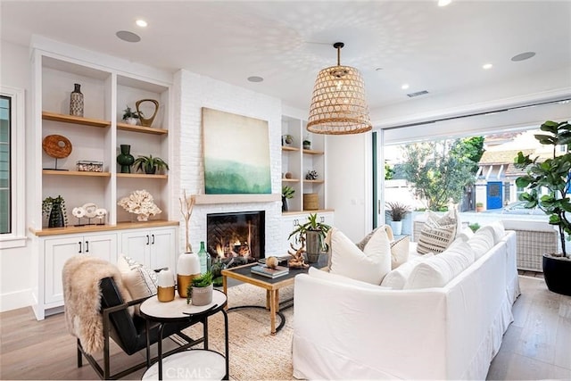 living room featuring built in features, light wood-type flooring, and a fireplace