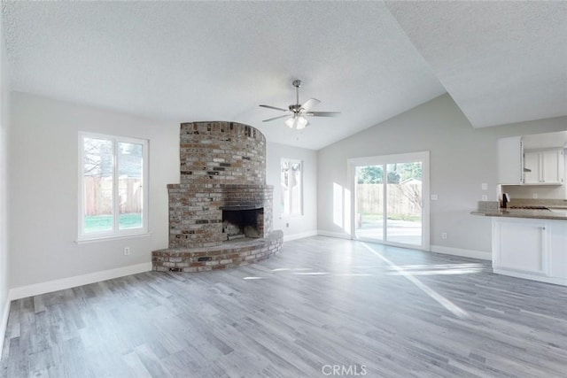 unfurnished living room with lofted ceiling, a fireplace, a textured ceiling, and light hardwood / wood-style floors