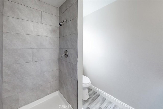 bathroom featuring wood-type flooring, toilet, and tiled shower