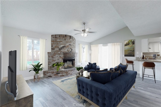 living room with vaulted ceiling, a textured ceiling, a fireplace, and light hardwood / wood-style flooring