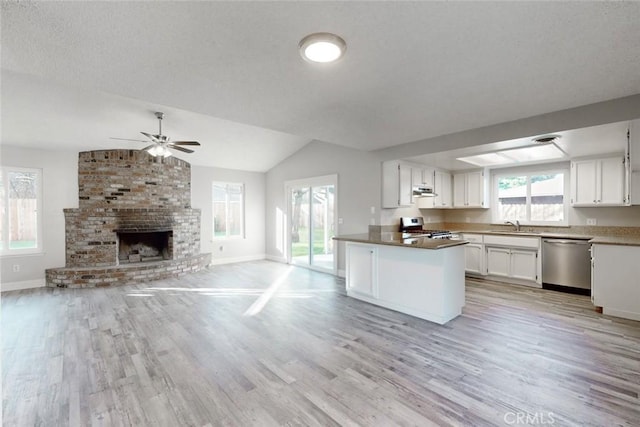 kitchen with sink, dishwasher, white cabinetry, stove, and a brick fireplace