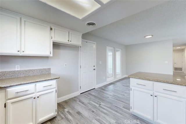 kitchen with light stone countertops, white cabinets, and light wood-type flooring