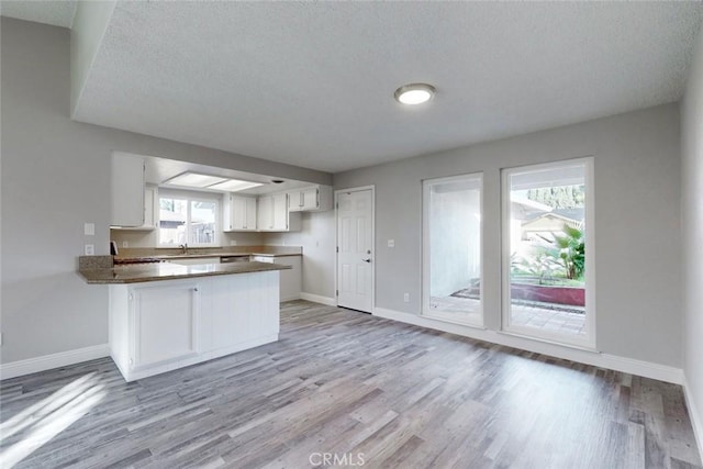 kitchen featuring white cabinetry, kitchen peninsula, a textured ceiling, and light wood-type flooring