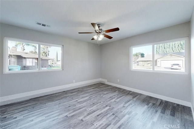 spare room featuring ceiling fan, wood-type flooring, and a healthy amount of sunlight