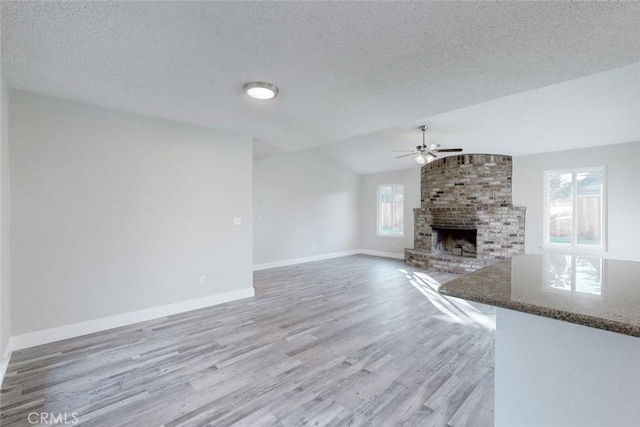 unfurnished living room featuring lofted ceiling, a fireplace, a textured ceiling, and a wealth of natural light