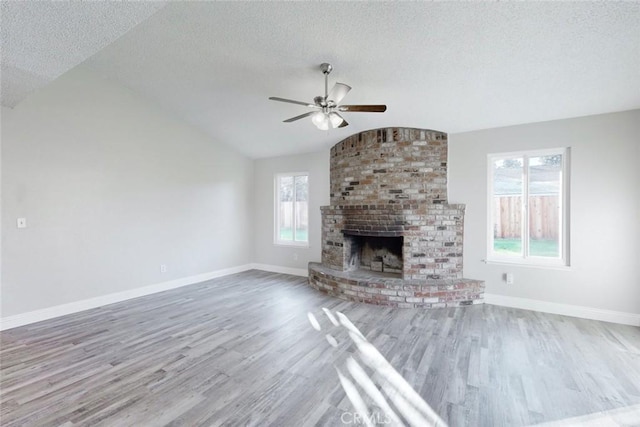 unfurnished living room featuring vaulted ceiling, a fireplace, hardwood / wood-style flooring, ceiling fan, and a textured ceiling