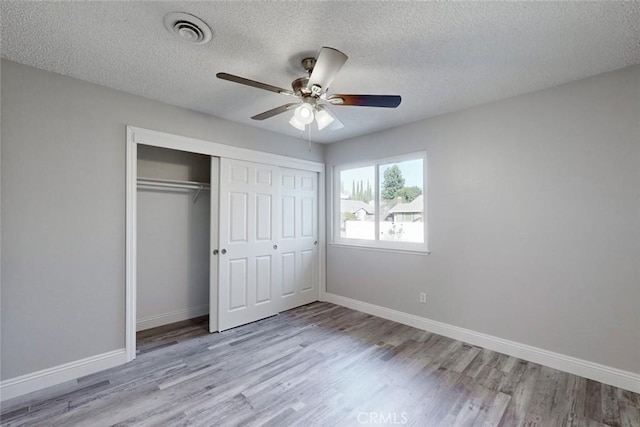 unfurnished bedroom featuring ceiling fan, a closet, a textured ceiling, and light wood-type flooring