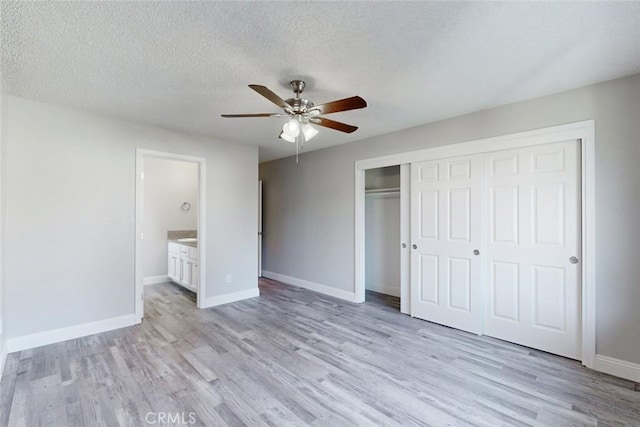 unfurnished bedroom with light wood-type flooring, ceiling fan, a textured ceiling, ensuite bath, and a closet