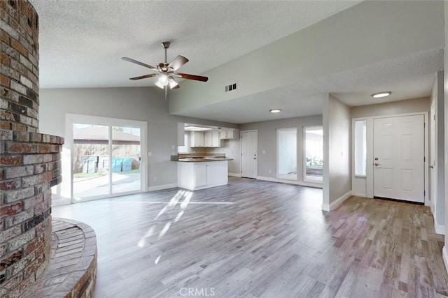 unfurnished living room featuring lofted ceiling, ceiling fan, light hardwood / wood-style flooring, and a textured ceiling