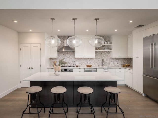 kitchen featuring pendant lighting, white cabinetry, stainless steel appliances, a kitchen island, and wall chimney exhaust hood