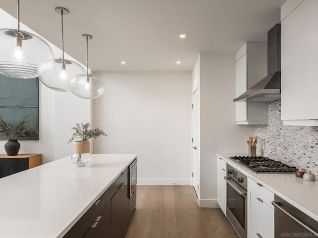 kitchen featuring appliances with stainless steel finishes, white cabinetry, backsplash, hanging light fixtures, and wall chimney range hood