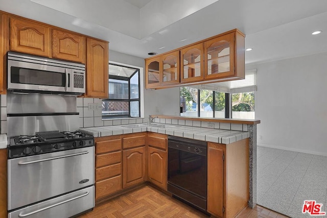 kitchen with appliances with stainless steel finishes, sink, tile counters, and kitchen peninsula