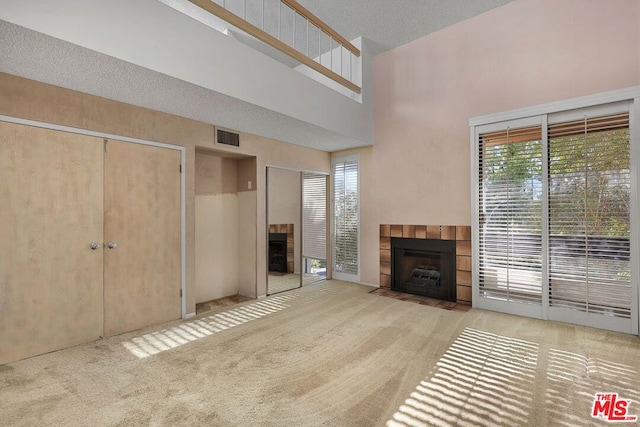 unfurnished living room with a tiled fireplace, a towering ceiling, and light carpet