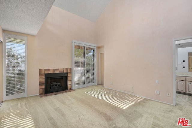 unfurnished living room with a tile fireplace, light carpet, a textured ceiling, and high vaulted ceiling