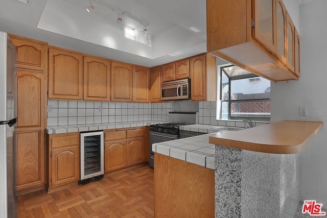 kitchen with kitchen peninsula, a raised ceiling, stainless steel appliances, beverage cooler, and decorative backsplash