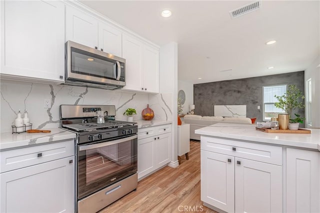 kitchen featuring tasteful backsplash, white cabinetry, appliances with stainless steel finishes, and light hardwood / wood-style floors