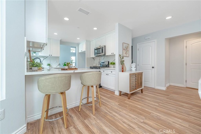 kitchen featuring appliances with stainless steel finishes, white cabinetry, a kitchen bar, kitchen peninsula, and light hardwood / wood-style flooring