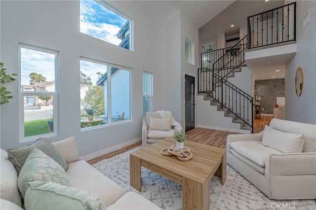 living room with a high ceiling, stairway, plenty of natural light, and light wood-style flooring