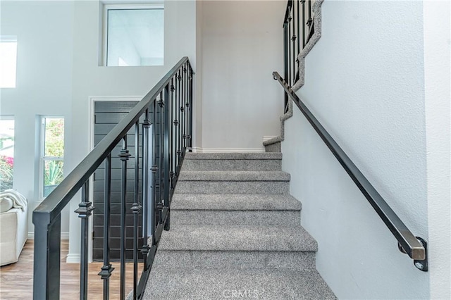 stairs featuring a towering ceiling and wood finished floors