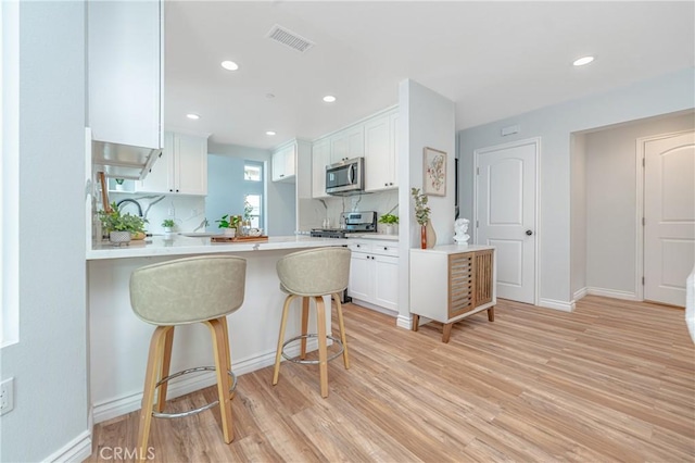 kitchen with visible vents, light countertops, appliances with stainless steel finishes, white cabinetry, and a peninsula