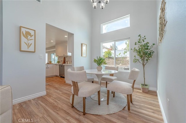 dining space with light wood-style floors, a chandelier, a high ceiling, and baseboards