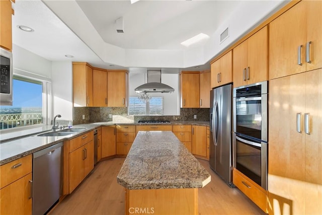 kitchen with wall chimney range hood, sink, stainless steel appliances, a center island, and light stone counters