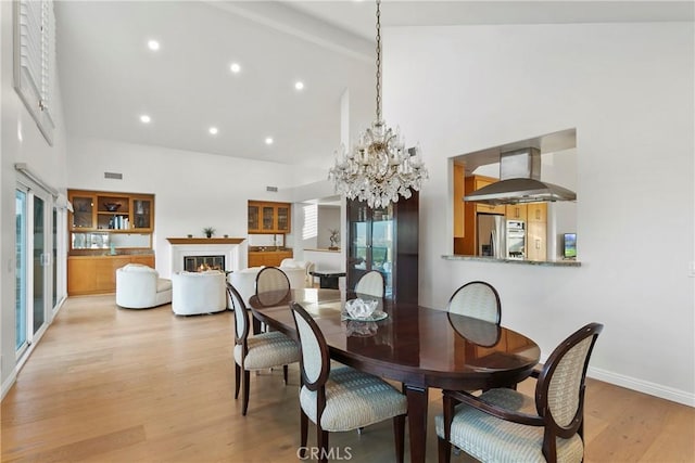 dining room with an inviting chandelier, high vaulted ceiling, and light hardwood / wood-style flooring