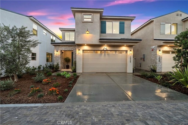 view of front of home featuring concrete driveway, an attached garage, stone siding, and stucco siding