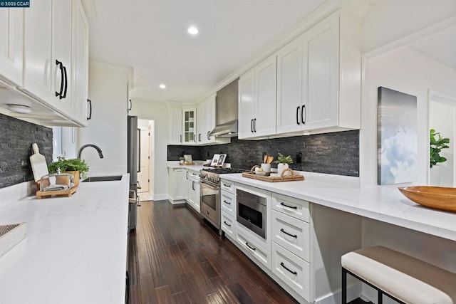 kitchen with dark hardwood / wood-style floors, white cabinets, stainless steel appliances, light stone countertops, and wall chimney range hood