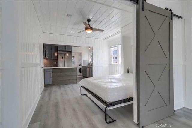 bedroom featuring washer / clothes dryer, a barn door, hardwood / wood-style floors, and ceiling fan