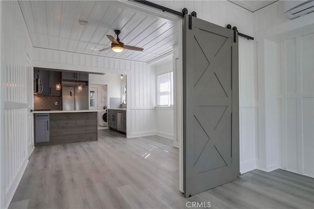 kitchen with washer / dryer, ceiling fan, a barn door, and light wood-type flooring