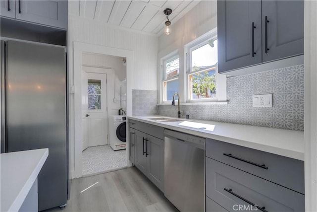 kitchen featuring sink, gray cabinets, hanging light fixtures, stainless steel appliances, and washer / dryer