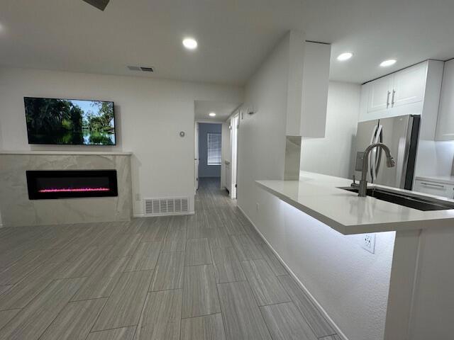 kitchen featuring stainless steel fridge, a fireplace, white cabinets, a kitchen bar, and kitchen peninsula