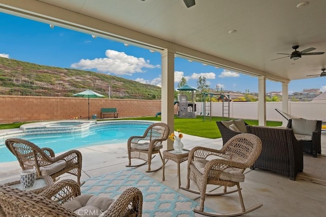 view of pool featuring a mountain view, an in ground hot tub, ceiling fan, a playground, and a patio