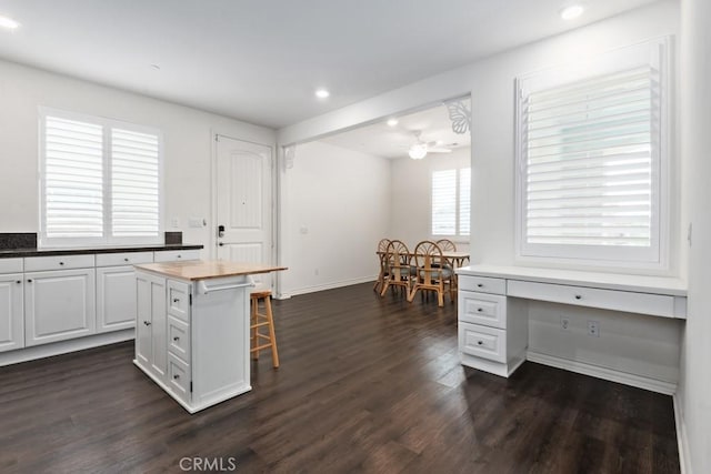 kitchen featuring a kitchen island, dark hardwood / wood-style floors, wood counters, white cabinetry, and a kitchen bar