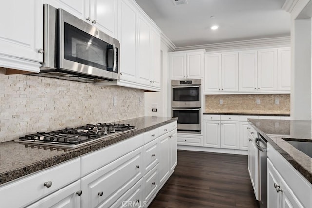 kitchen featuring dark wood-type flooring, dark stone countertops, white cabinets, stainless steel appliances, and backsplash