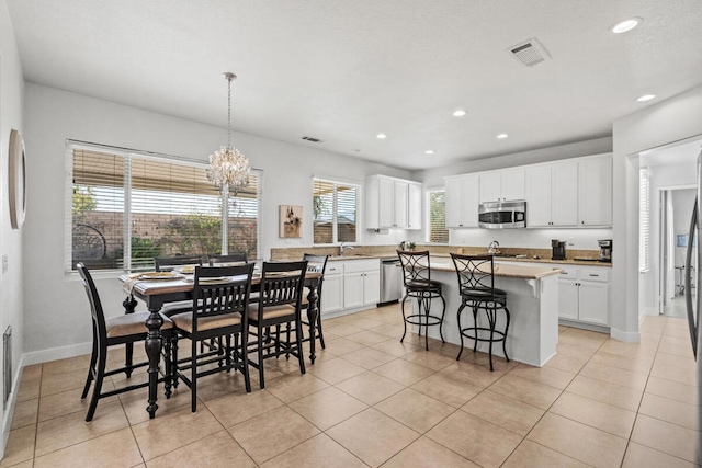 kitchen with light tile patterned floors, a kitchen island, pendant lighting, stainless steel appliances, and white cabinets