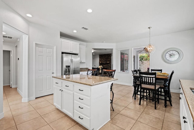 kitchen featuring decorative light fixtures, white cabinetry, stainless steel fridge, a kitchen breakfast bar, and a center island