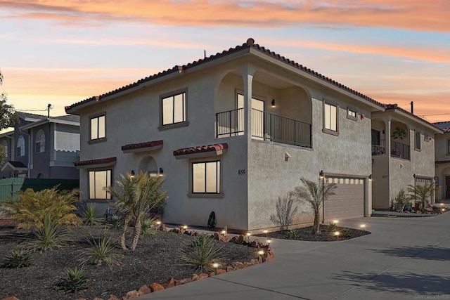 property exterior at dusk with a garage and a balcony