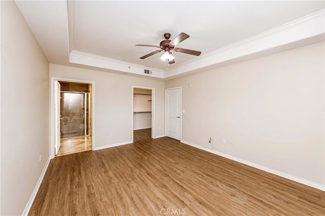 unfurnished bedroom featuring hardwood / wood-style floors, ensuite bathroom, ornamental molding, a walk in closet, and a raised ceiling