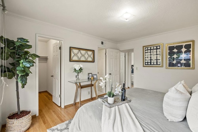 bedroom with crown molding, a spacious closet, a textured ceiling, and light hardwood / wood-style flooring