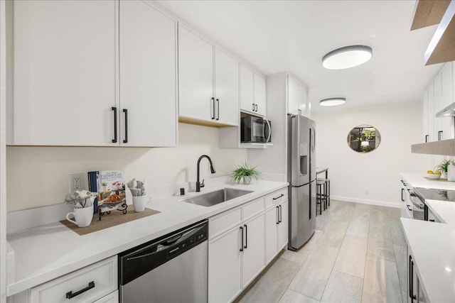 kitchen with white cabinetry, appliances with stainless steel finishes, sink, and light wood-type flooring