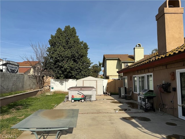 view of patio featuring a hot tub, a grill, a shed, a fenced backyard, and an outdoor structure