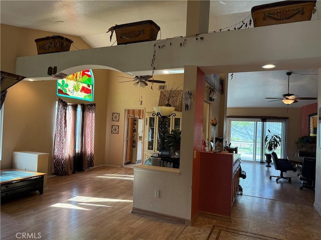 kitchen featuring ceiling fan, high vaulted ceiling, arched walkways, wood finished floors, and baseboards