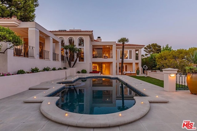 pool at dusk featuring an in ground hot tub and a patio