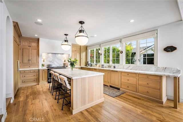 kitchen with decorative light fixtures, a kitchen bar, a center island, gas stove, and light wood-type flooring