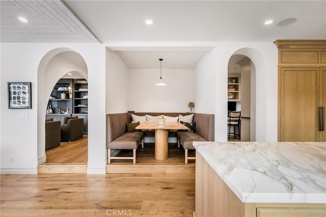 kitchen featuring decorative light fixtures, light hardwood / wood-style floors, light stone countertops, light brown cabinets, and built in shelves