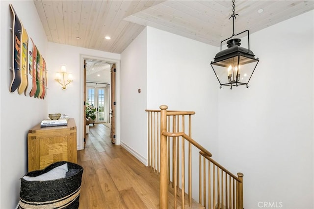 hallway with an inviting chandelier, light hardwood / wood-style flooring, and wooden ceiling