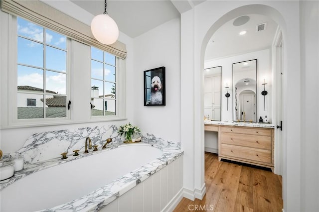 bathroom with vanity, a bath, and wood-type flooring